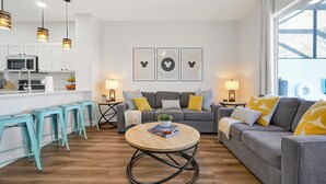 Una sala de estar moderna con un sofá gris, una mesa de centro redonda y una cocina con alacenas blancas y un microondas.
