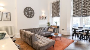 A modern living room with a sectional sofa, a round coffee table, and a dining area with a table and chairs. - Rowley House at Stone Cross Mansion (Ulverston)