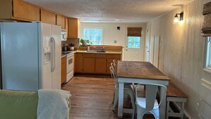 A compact kitchen with wooden cabinets, a white refrigerator, and a dining table with chairs.