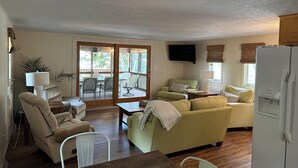 A living room with a wooden table, beige sofas, a TV, and a sliding glass door leading to a patio.