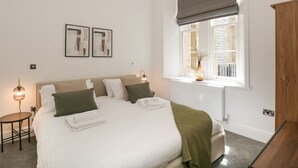 A neatly arranged bedroom with a large bed, bedside lamps, a window with a view, and a wooden cabinet.