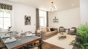 A modern living room with a dining area, featuring a sofa set, armchairs, a coffee table, and a dining table set for four.