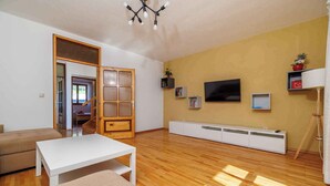 A spacious living room with a wooden floor, a white sofa, a white coffee table, a TV mounted on the wall, and a bookshelf. - Holiday apartment with 4 bedrooms and a balcony (Crikvenica)