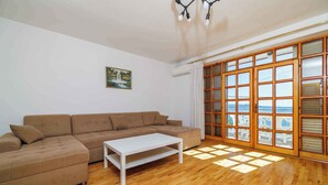 A living room with a brown sectional sofa, a white coffee table, and a large sliding glass door with a view. - Holiday apartment with terrace and air conditioning (Crikvenica)