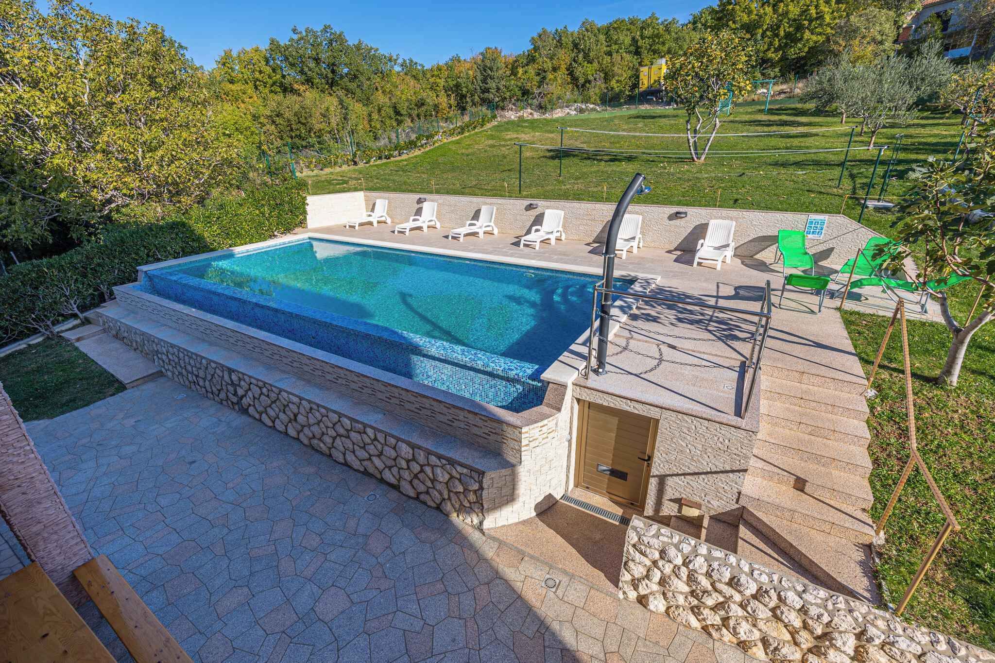 A swimming pool with a stone deck, lounge chairs, and a wooden deck area.