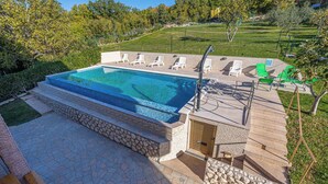 A swimming pool with a stone deck, lounge chairs, and a wooden deck area. - Holiday apartment with terrace and air conditioning (Crikvenica)