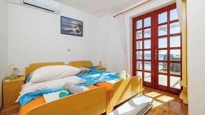 A room with a wooden bed, a nightstand, a lamp, and a large window with curtains. - Holiday apartment with terrace and air conditioning (Crikvenica)