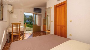 A bedroom with a bed, a small table, and a chair. There is a door leading to a balcony with a view of greenery.