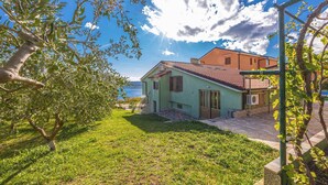 A house with a tiled roof, a small garden, and a view of the sea.