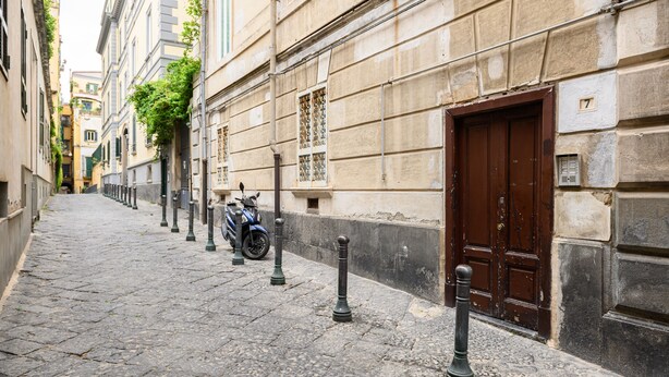 Una estrecha calle adoquinada flanqueada por edificios históricos, una puerta marrón y un scooter estacionado.