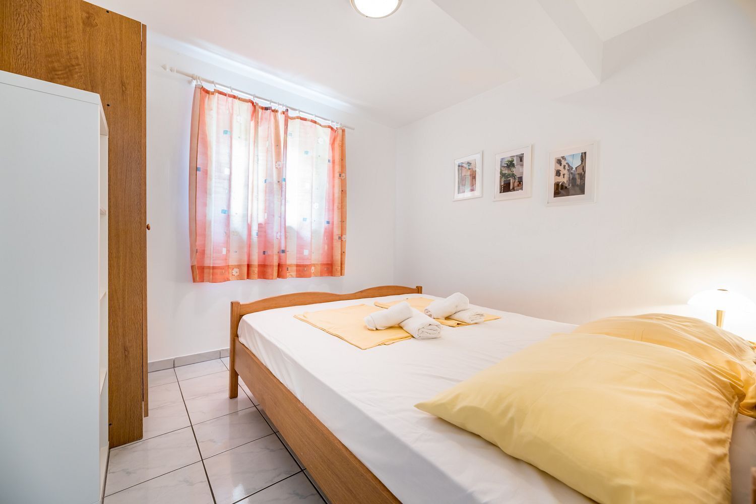 Ein Schlafzimmer mit einem Bett, einem Fenster mit Vorhängen, einer Tür und einer Wand mit Bildern.