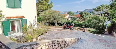 A paved driveway leading to a building with a tiled roof and green shutters.