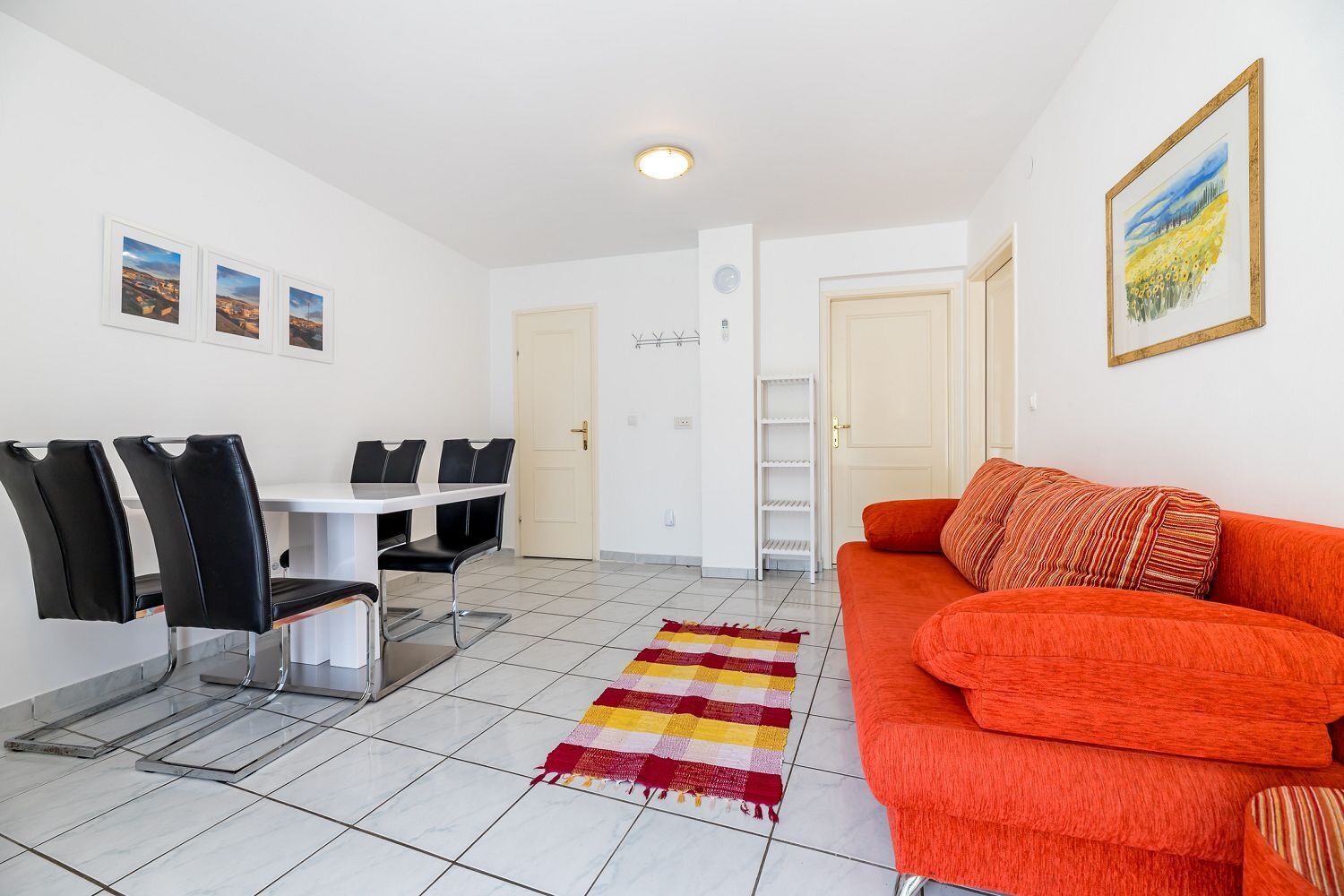 A living room with a red sofa, a dining table with chairs, and a colorful rug.