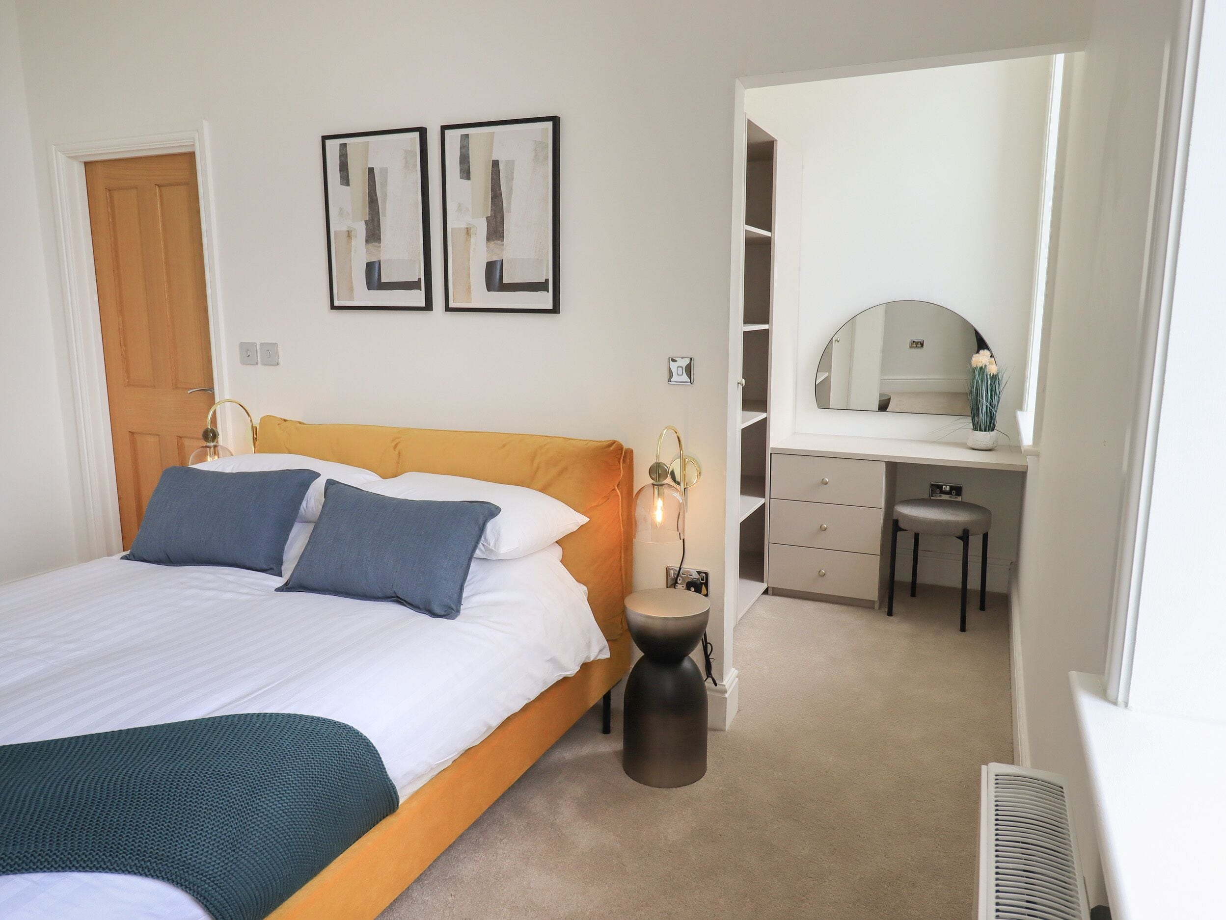 A bedroom with a bed, bedside table, lamp, and a desk with a chair.