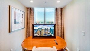 Quarto de hotel com uma janela grande, televisão de tela plana, mesa de madeira e controle remoto.