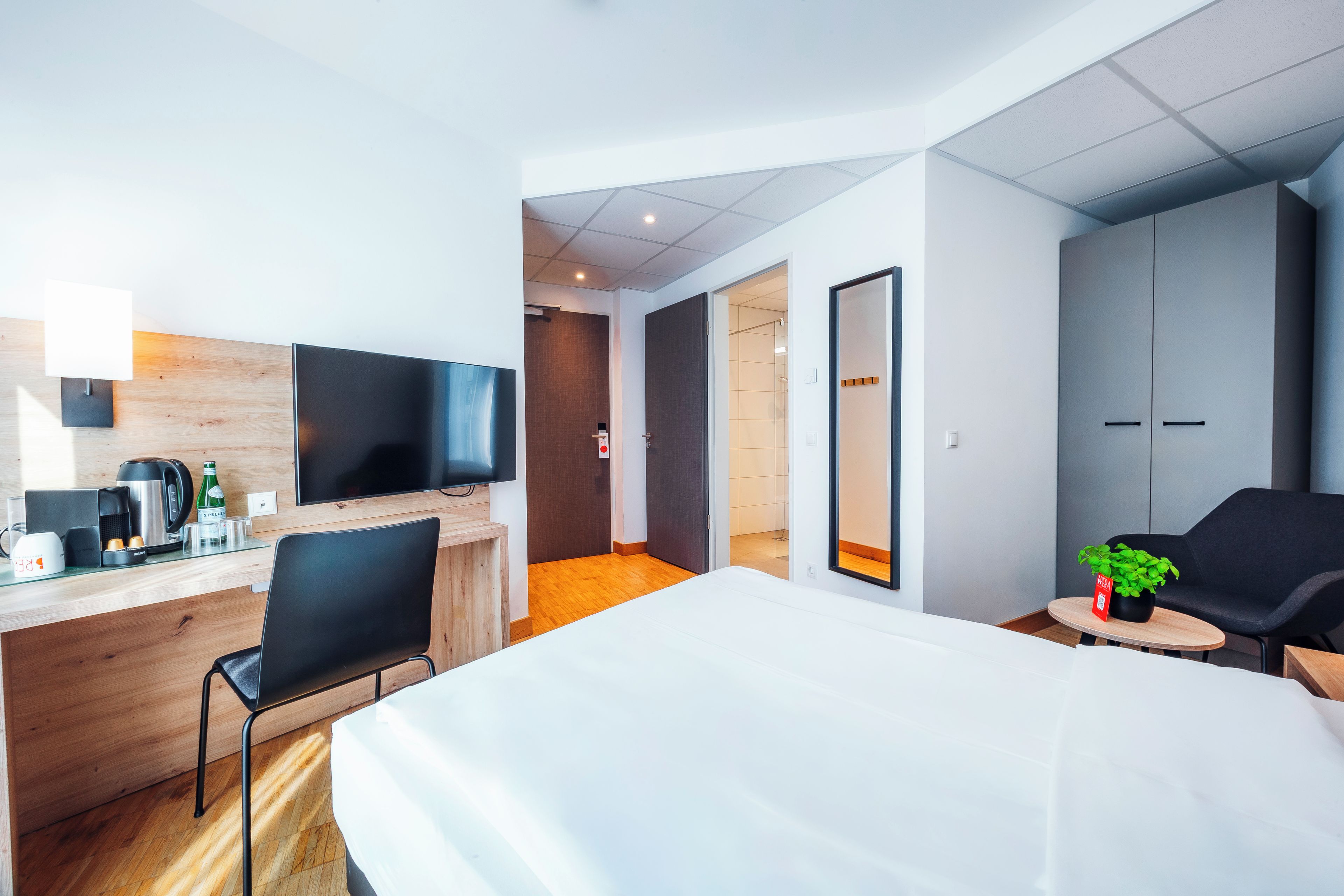 Hotellihuone, jossa on sänky, työpöytä kahvinkeittimellä, televisio ja oleskelualue, jossa on myös kasvi.