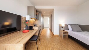 Una habitación de hotel moderna con un escritorio de madera, una cama, un televisor y una kitchenette.