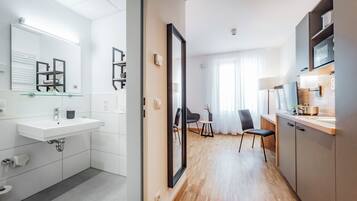 A modern hotel room with a bathroom, a dining area, and a kitchenette.
