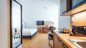Habitación de hotel moderna con cama, escritorio, silla, televisor y cocina equipada con estufa y lavaplatos, además de suelo de madera.