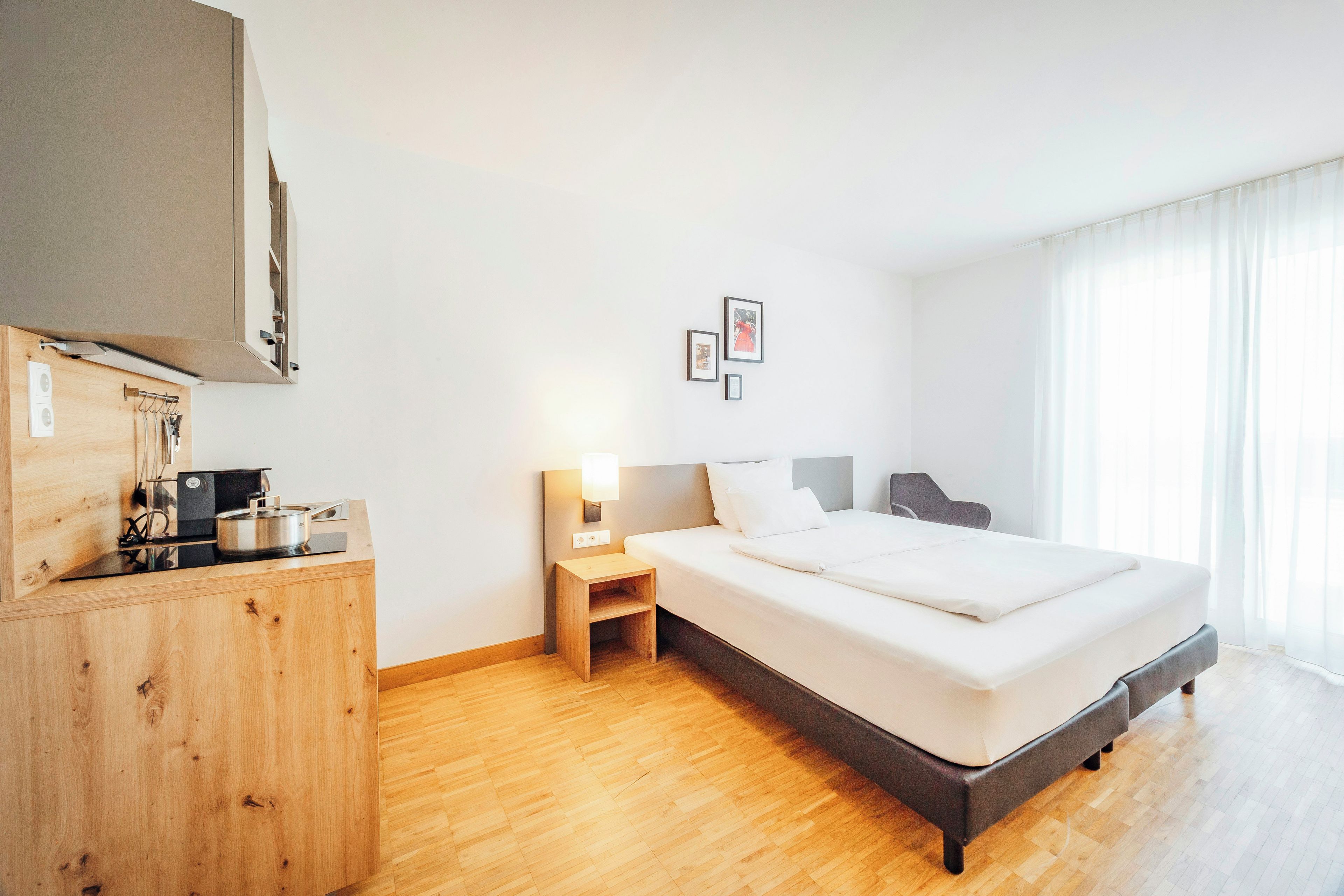 A hotel room with a bed, bedside table, and a wooden cabinet with a stove.