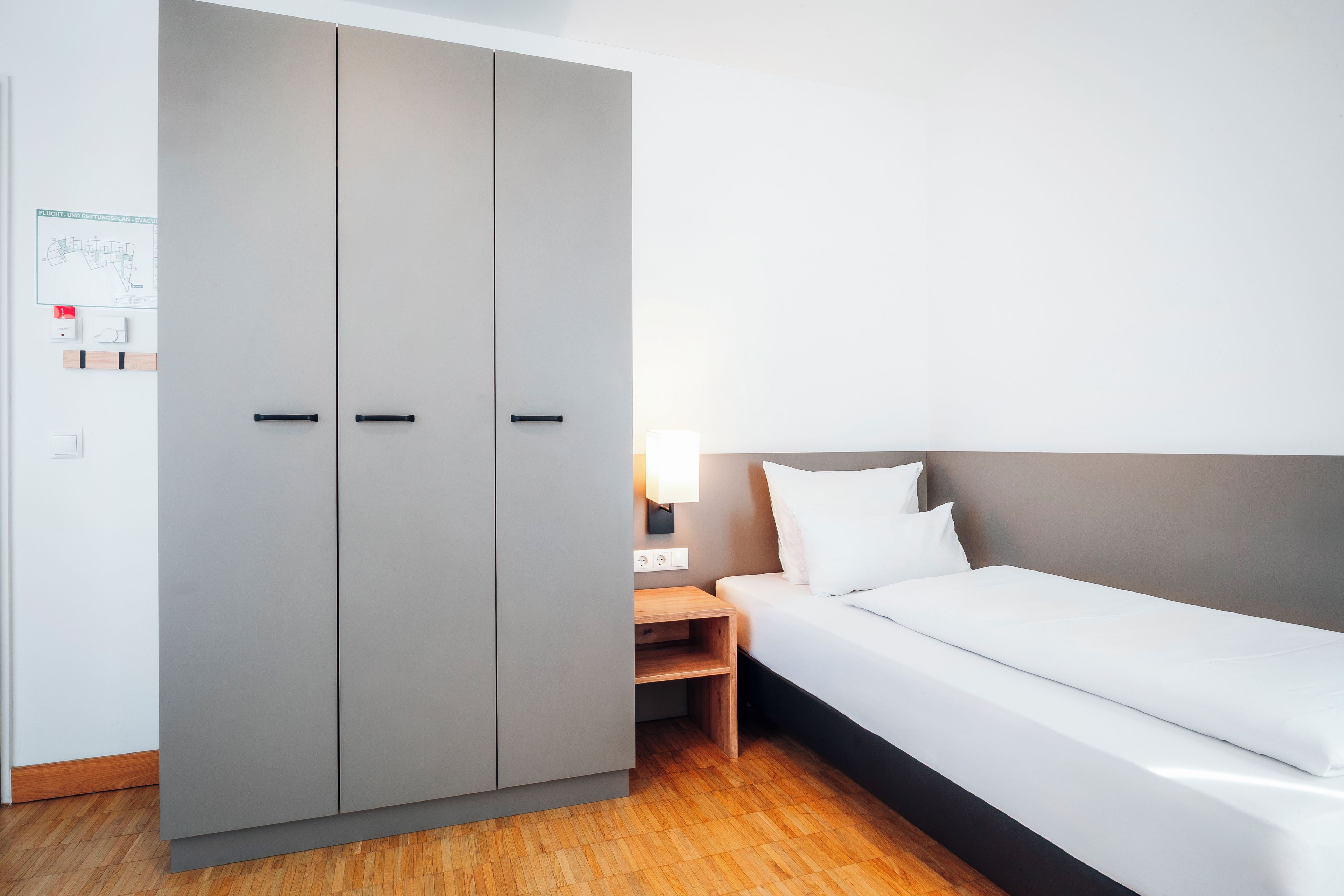 Una habitación de hotel con una cama, una mesita de noche, una lámpara y un armario.