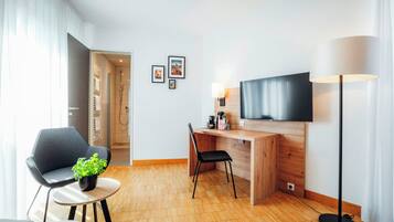 Une chambre d’hôtel moderne avec un bureau en bois, un téléviseur à écran plat, une chaise, une petite table avec une plante et un lampadaire.