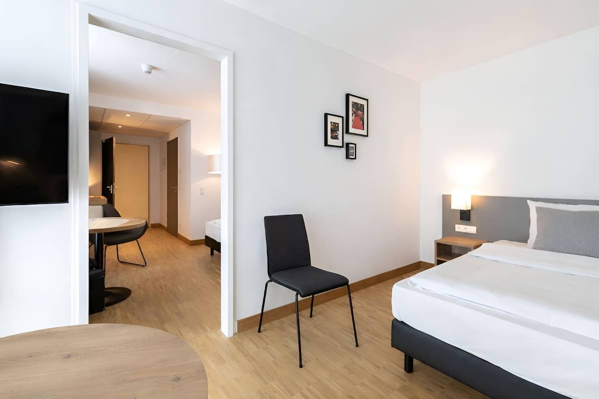 A hotel room with a bed, a chair, a desk, and a TV.