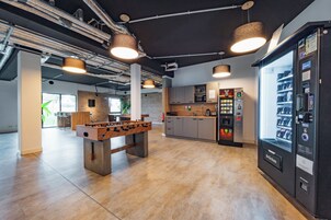 Un espacio interior moderno con mesa de futbolín, cafetera y máquina expendedora.