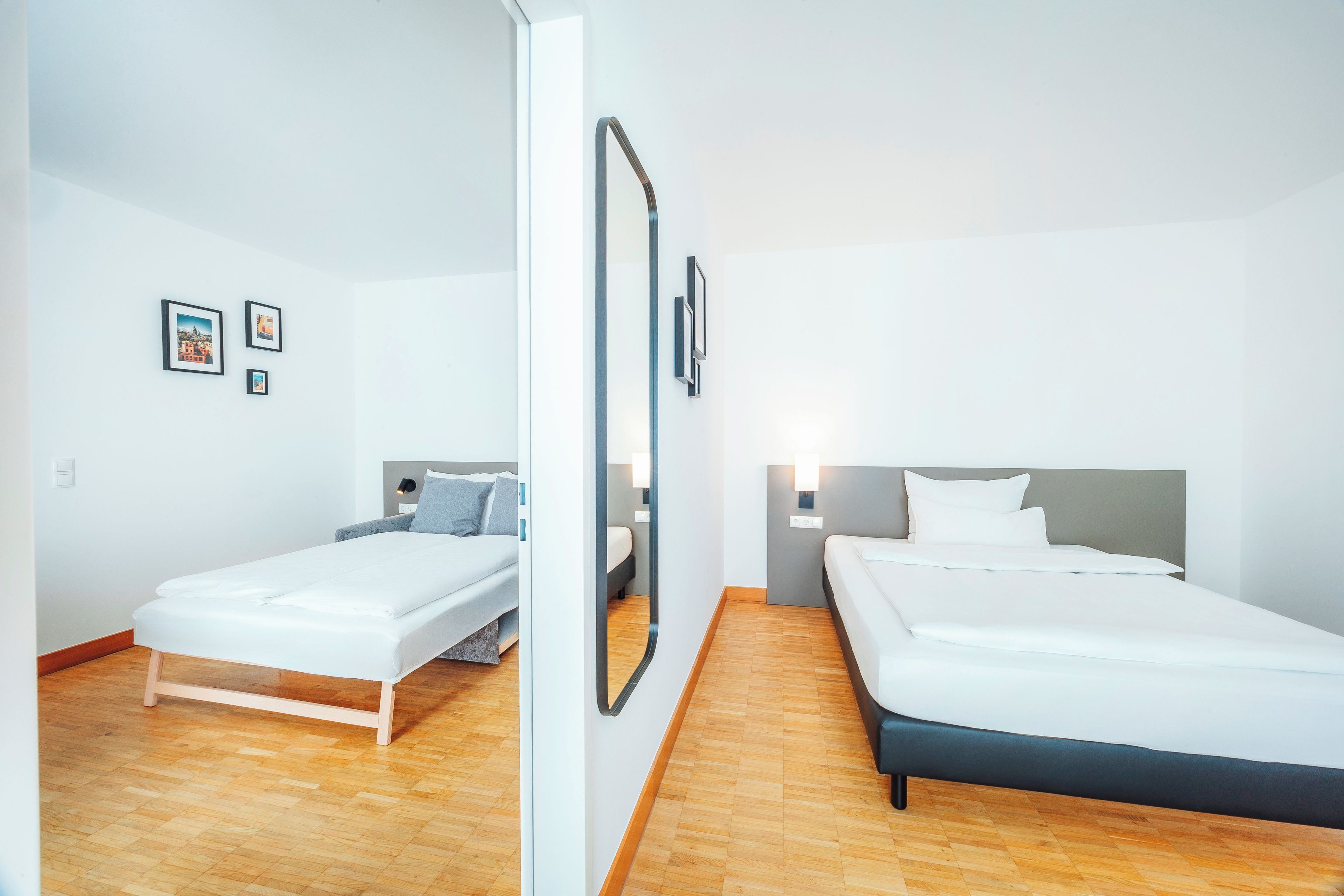 Een moderne hotelkamer met twee eenpersoonsbedden, een houten vloer en een grote spiegel aan de muur.