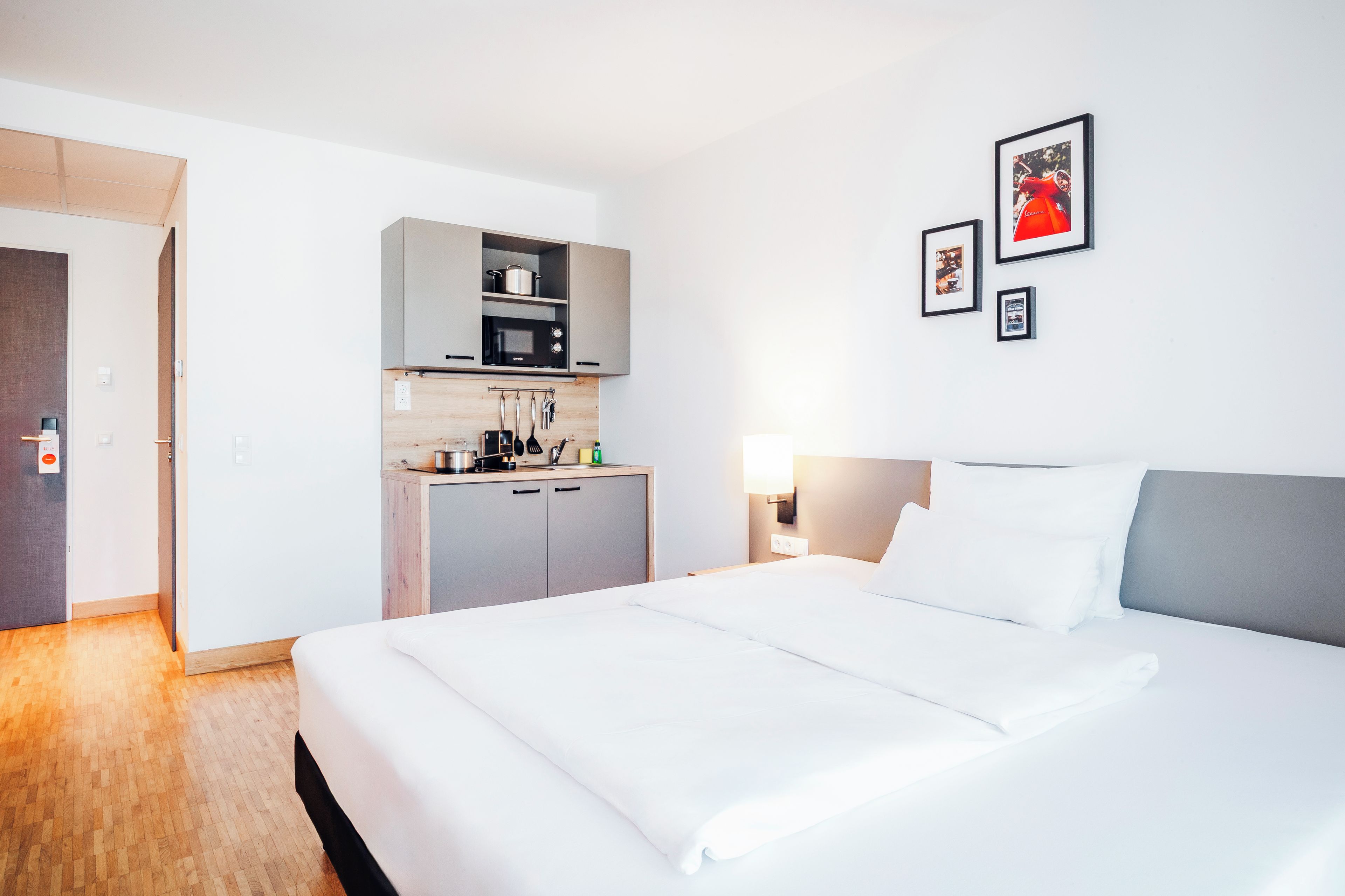 Una habitación de hotel con una cama, kitchenette y una lámpara fijada a la pared.