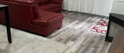 Un salon avec un canapé en cuir rouge, un plancher en bois et un rideau blanc.