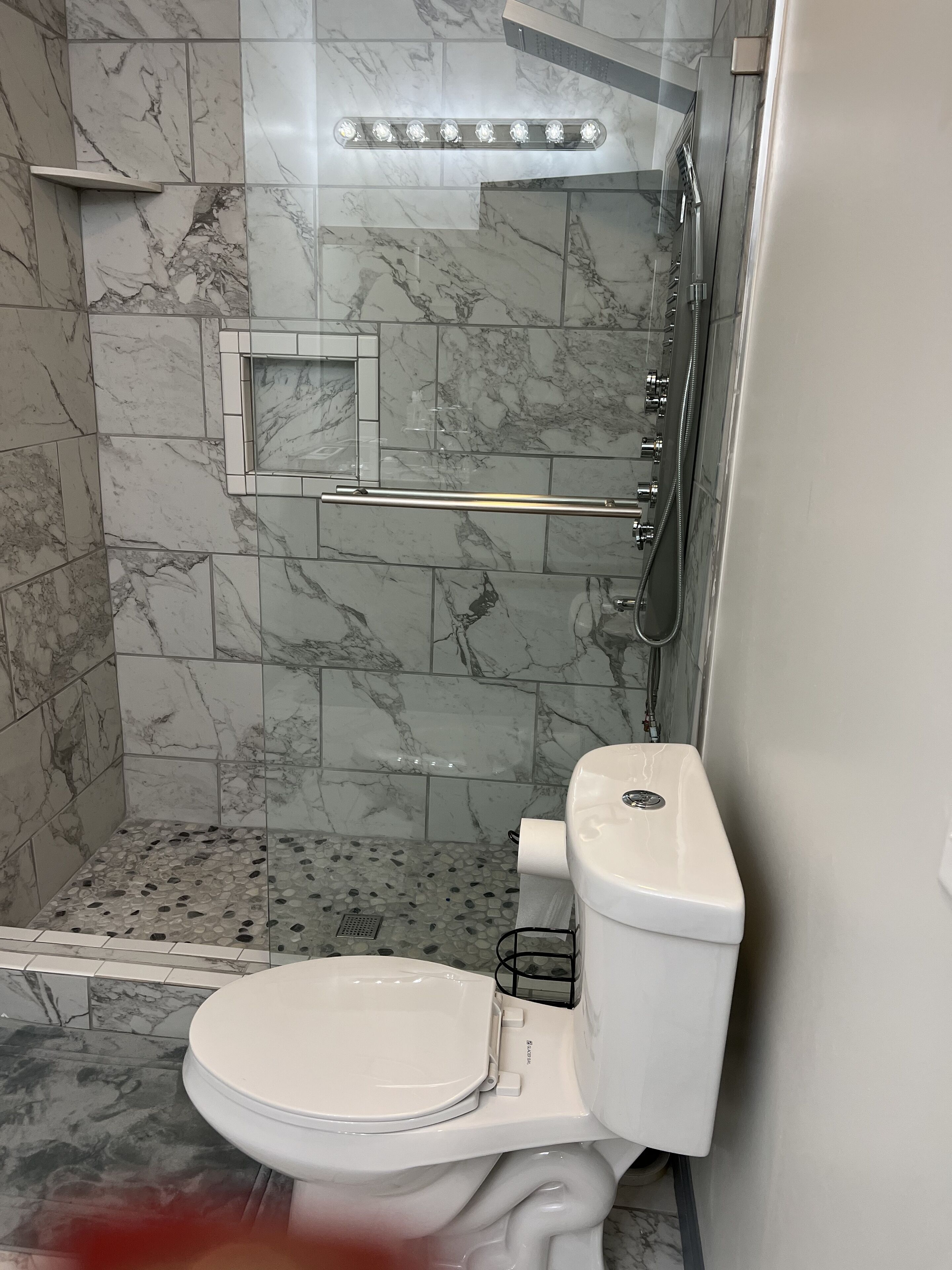 Een moderne badkamer met een marmeren vloer, een douchecabine van glas, een toilet en een handgreep.
