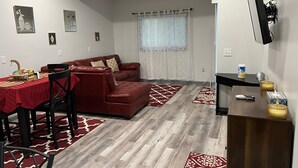 A living room with a red sofa, a dining table with chairs, and a TV mounted on the wall. - Lovely 2 bedroom rental unit with free parking (Columbus)