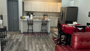 A modern kitchen with white cabinets, a central island with stools, a dining area with a red sofa, and a grey door. - Lovely 2 bedroom rental unit with free parking (Columbus)