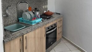 Een compacte keuken met houten kastjes, een granieten aanrechtblad, een spoelbak, een fornuis en een vaatwasser.