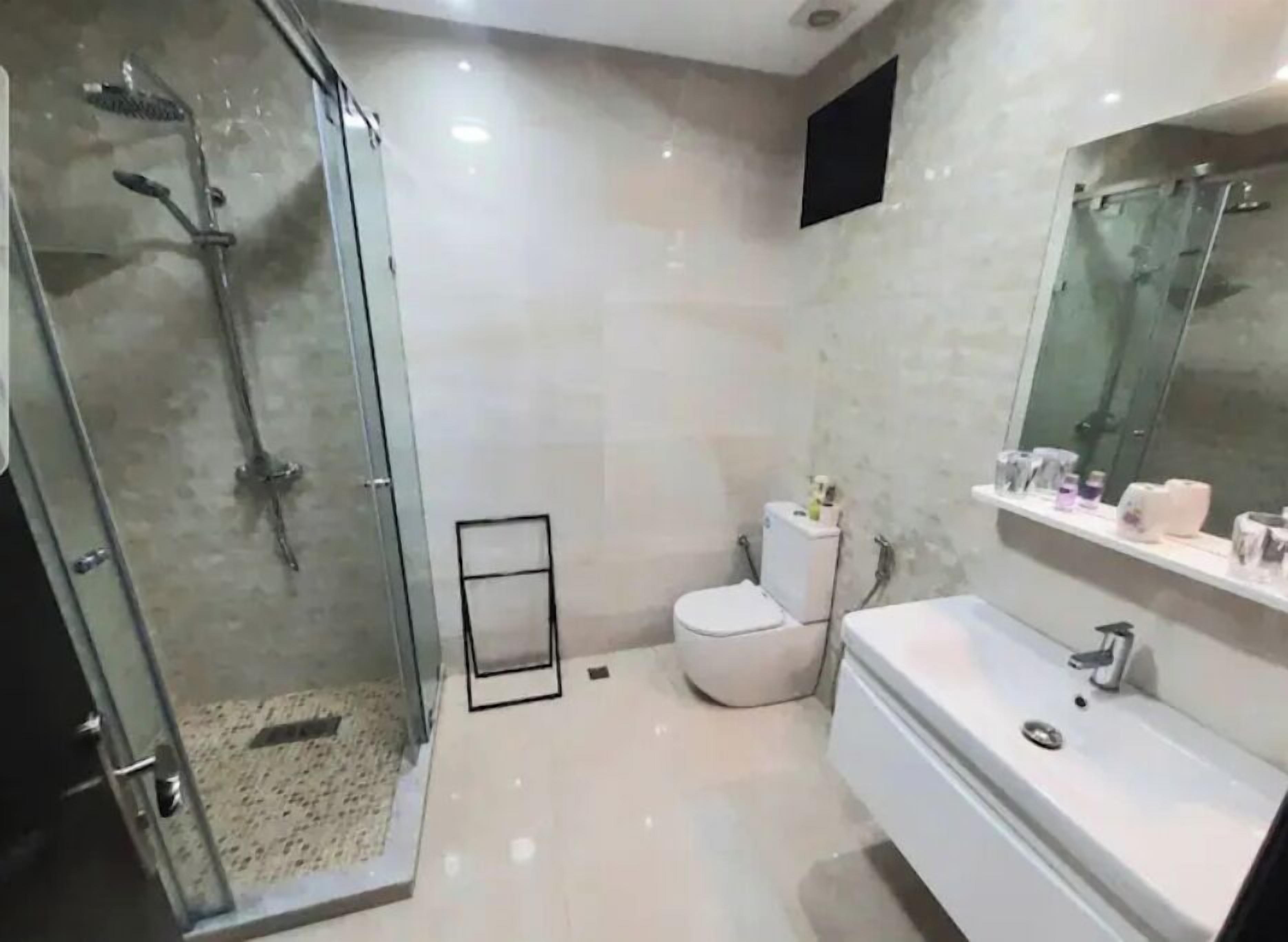 A modern bathroom with a glass-enclosed shower, a white toilet, and a large mirror above the sink.