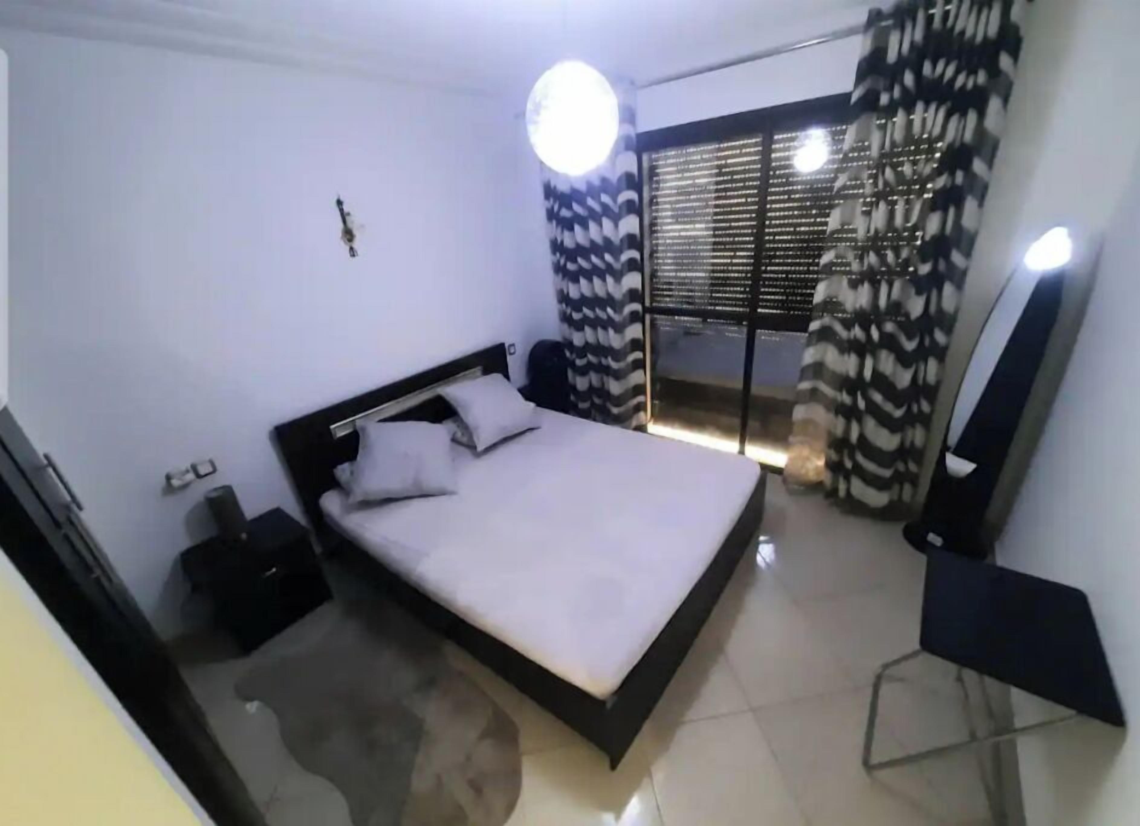 Une chambre à coucher moderne avec un lit, une table de chevet, un miroir et une fenêtre avec des rideaux.