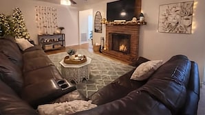 A living room with a fireplace, leather sofas, a coffee table, and a ceiling fan. - Spacious 4BR Near Pinehurst | Fire Pit + Games (Southern Pines)