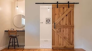 A room with a wooden floor, a desk with a chair, a round mirror, and a sliding barn-style door. - Spacious 4BR Near Pinehurst | Fire Pit + Games (Southern Pines)