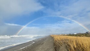 A beach with a visible rainbow, waves, and a grassy area with houses in the background.