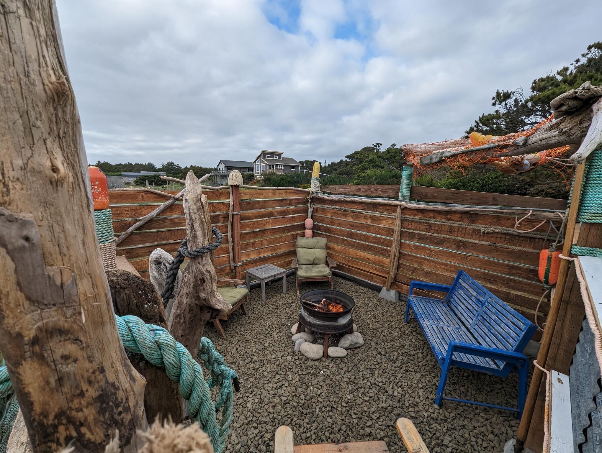 A rustic outdoor seating area with a fire pit, benches, and a wooden fence.