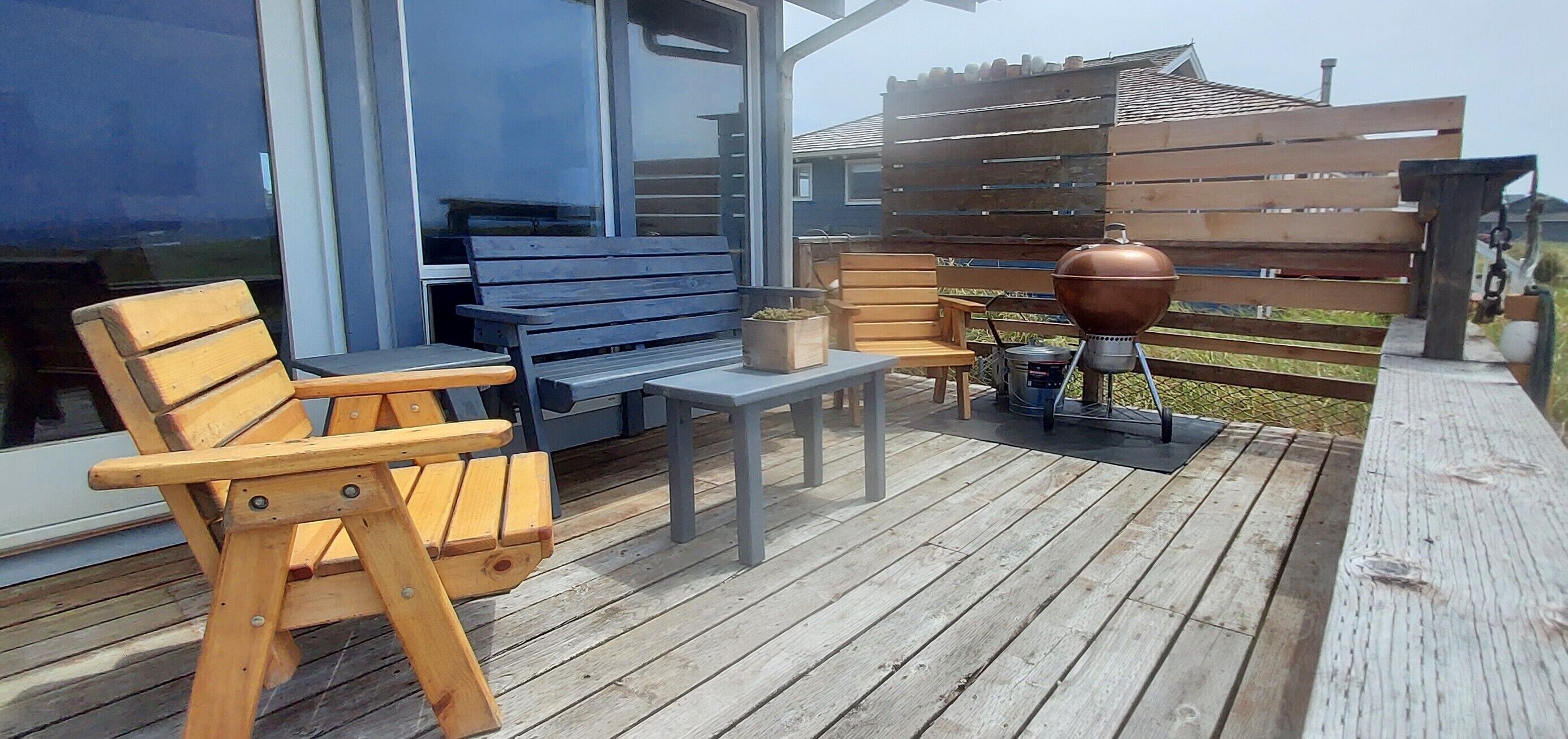 Une terrasse en bois avec un barbecue, des chaises en bois et une table.