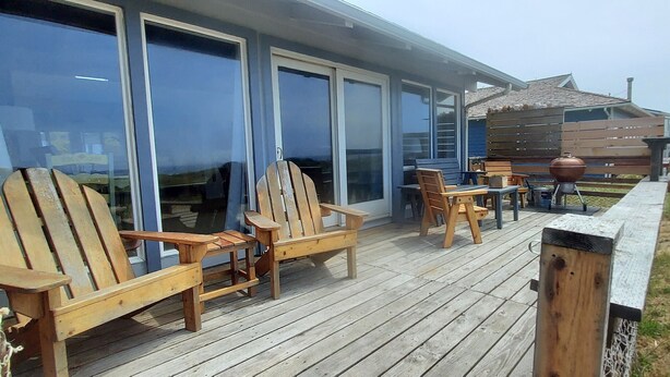 A wooden deck with Adirondack chairs and a table, a barbecue grill, and a wooden fence.