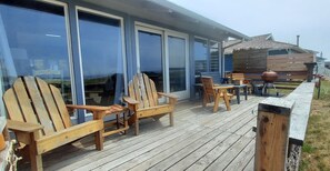 A wooden deck with Adirondack chairs and a table, a barbecue grill, and a wooden fence.