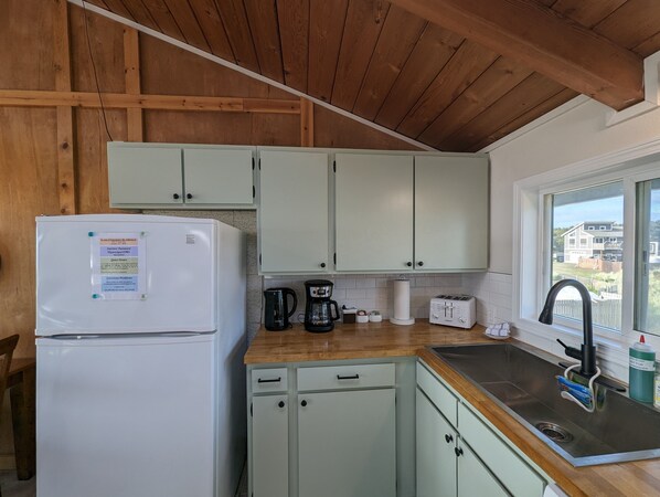 A kitchen with wooden beams, a refrigerator, a coffee maker, a toaster, and a window with a view of houses.