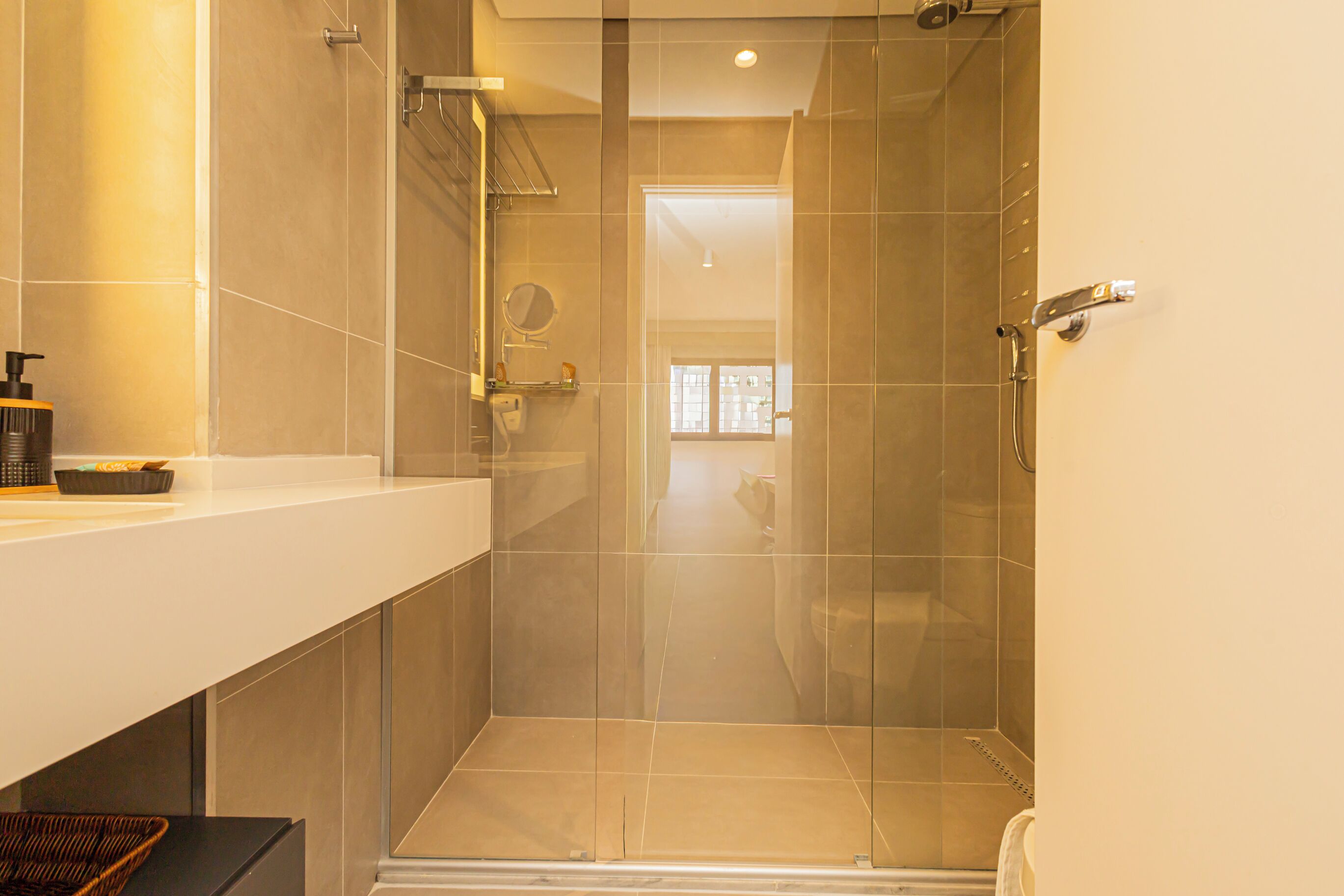 A modern bathroom with a glass shower enclosure, a white countertop, and a visible door leading to another room.