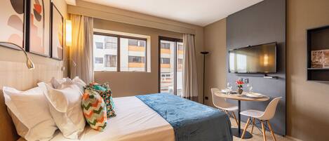 A hotel room with a bed, a desk, a chair, a television, and a window.