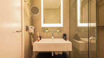 A bathroom with a white sink, a glass shower enclosure, a mirror above the sink, and a small shelf with plants.