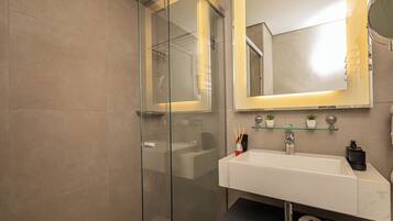 Un baño moderno con cabina de ducha de vidrio, un lavabo blanco e iluminación integrada en el espejo.
