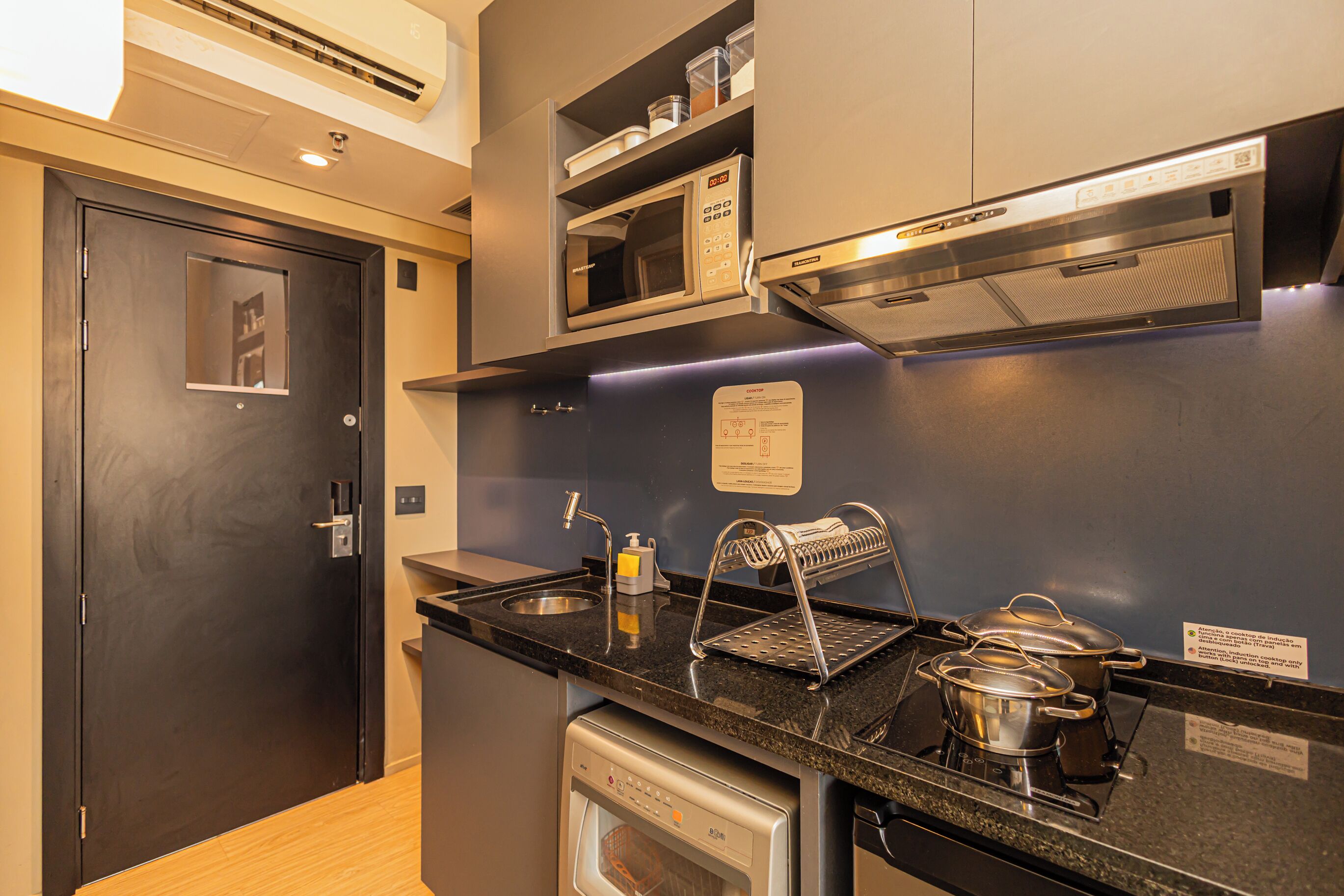 A compact kitchen with a microwave, stove, sink, and dish drying rack.